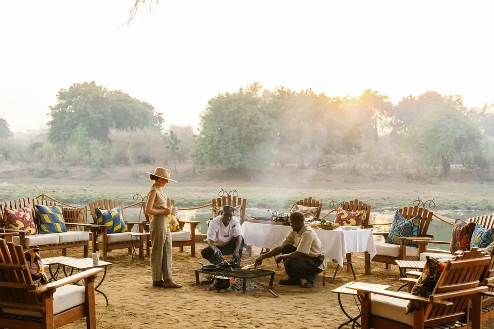 Campfire breakfast on the riverbank at Chongwe Camp with staff preparing food, Lower Zambezi National Park, Zambia