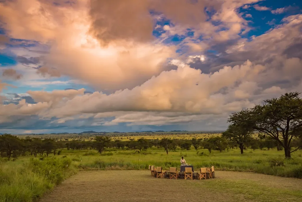 Dunia Camp staff preparing sundowners by the firepit with sweeping Serengeti views