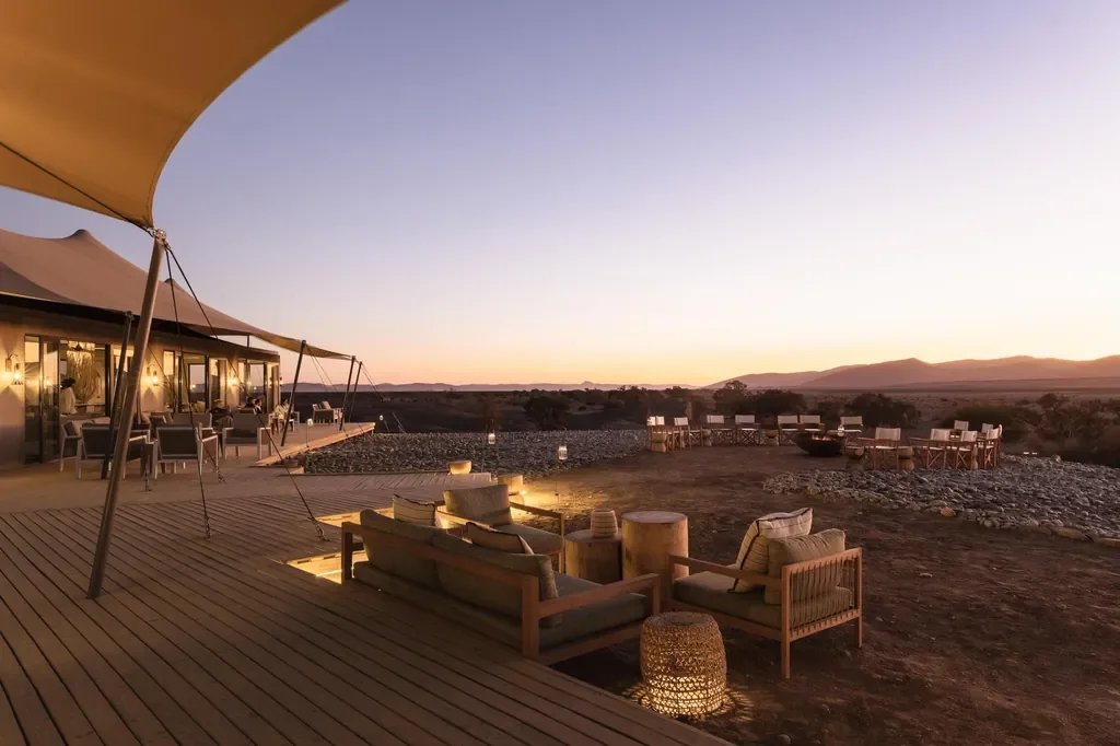 Kulala Desert Lodge deck lounge at twilight with campfire and desert horizon