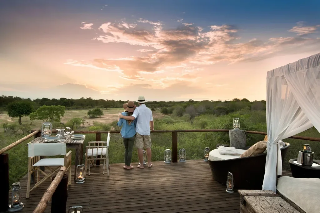 Couple watching a golden sunset from Chalkley Treehouse deck overlooking the Sabie River floodplain, Lion Sands, Sabi Sand, South Africa.