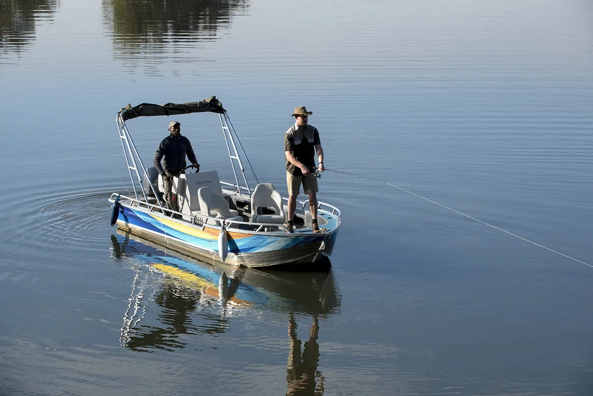 Guest fishing from a boat on a broad river at sunset in Southern Africa on Zambezi River in Zambia