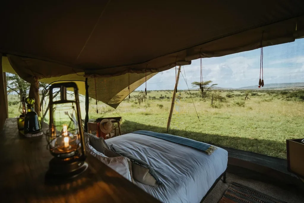 Open-sided Usawa tent bedroom with lanterns and sweeping Serengeti savannah view