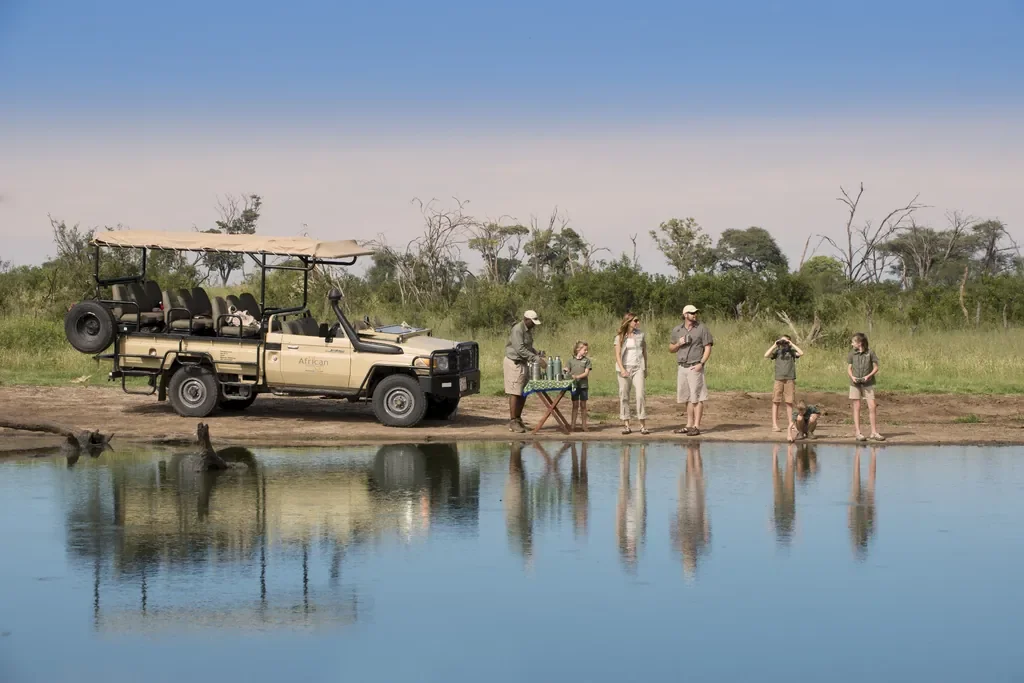 Family safari stop by a pan with guide and game viewer, Somalisa Acacia Hwange