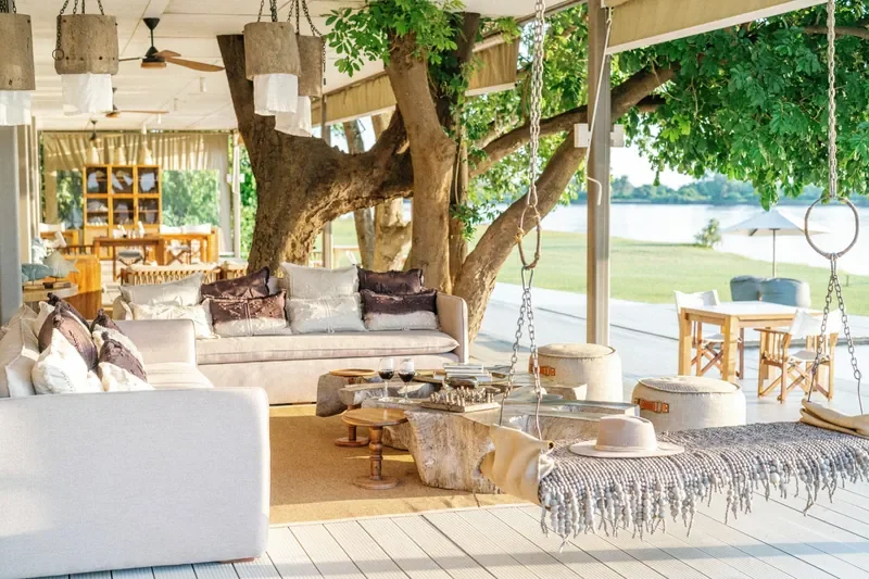 Open-air lounge with hanging daybeds and tree-shaded seating at Time + Tide Chinzombo, Luangwa River outlook, South Luangwa, Zambia