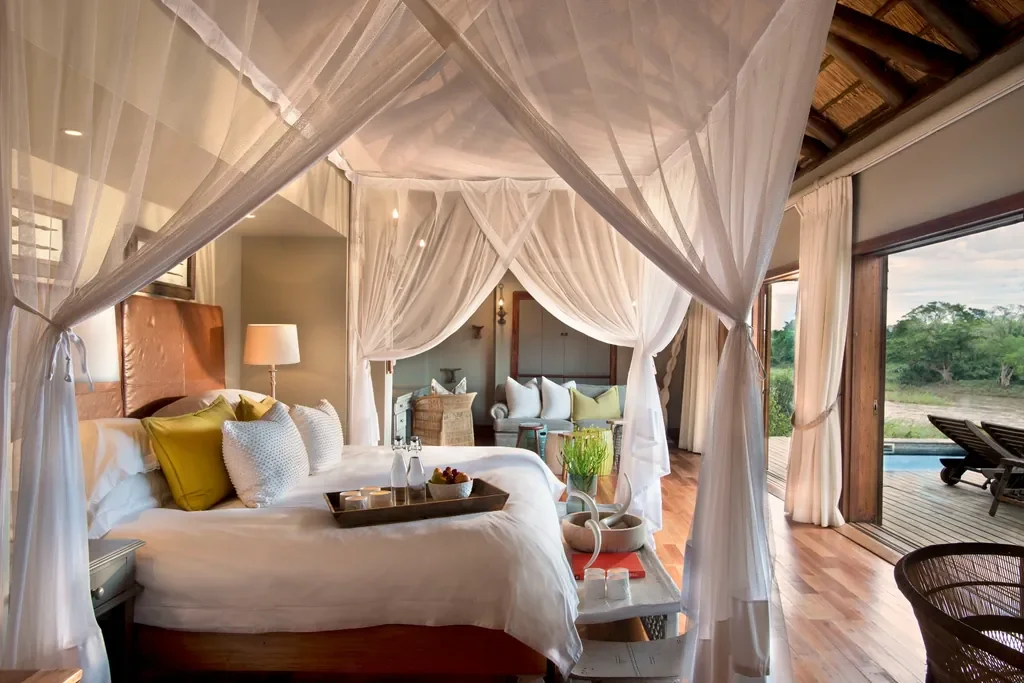 Suite bedroom with canopy bed opening to private deck at Lion Sands Narina Lodge, Greater Kruger South Africa