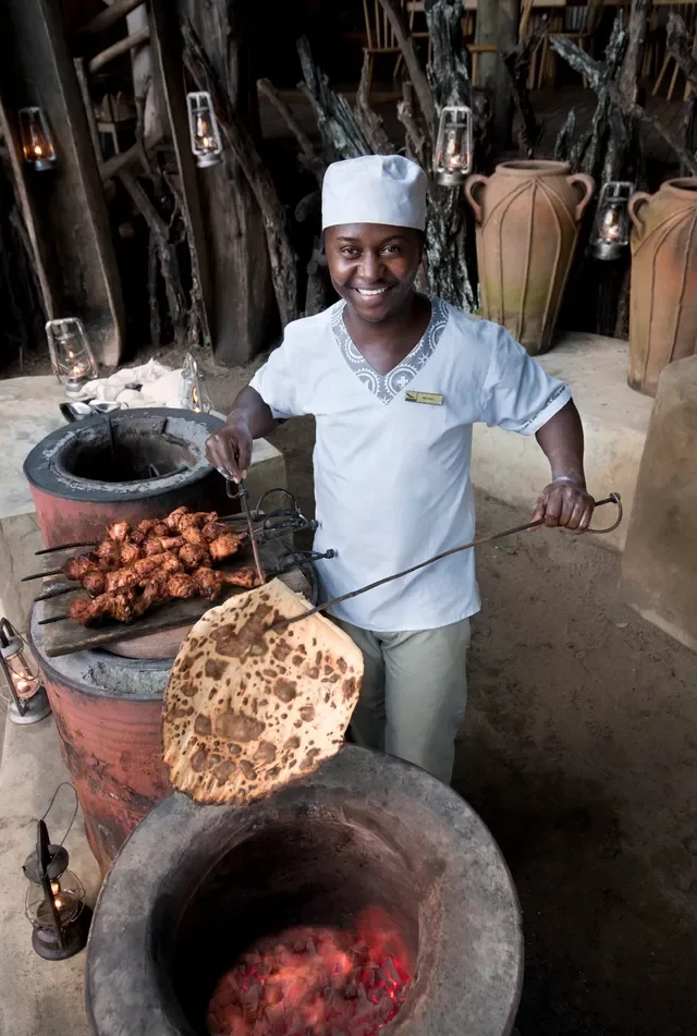 Lake Manyara Tree Lodge, Tanzania – chef–butler grilling tandoori skewers beside a clay oven