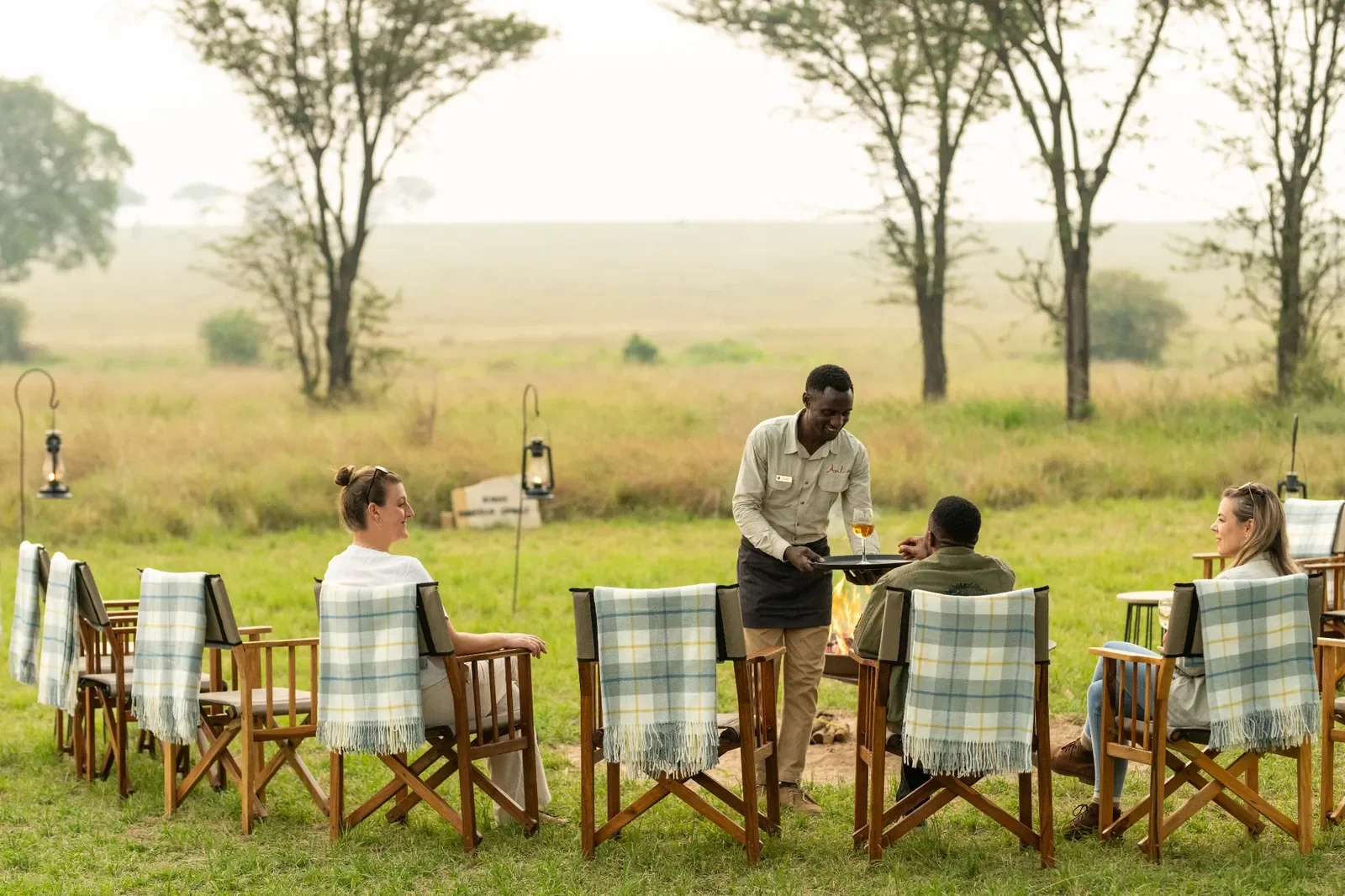 Sundowners at Ubuntu Migration Camp, chairs around the fire with drinks and views over the Serengeti plains, Tanzania