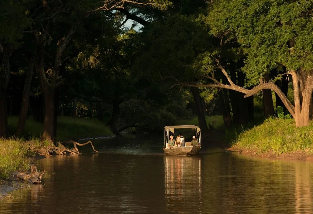 Boat safari cruising a shaded stretch of the Luangwa River in South Luangwa National Park, Zambia