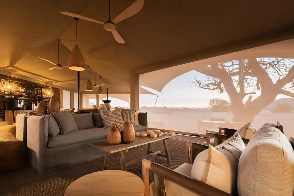 Warm lounge and dining interior at Desert Rhino Camp, candlelit table setting, Damaraland Namibia