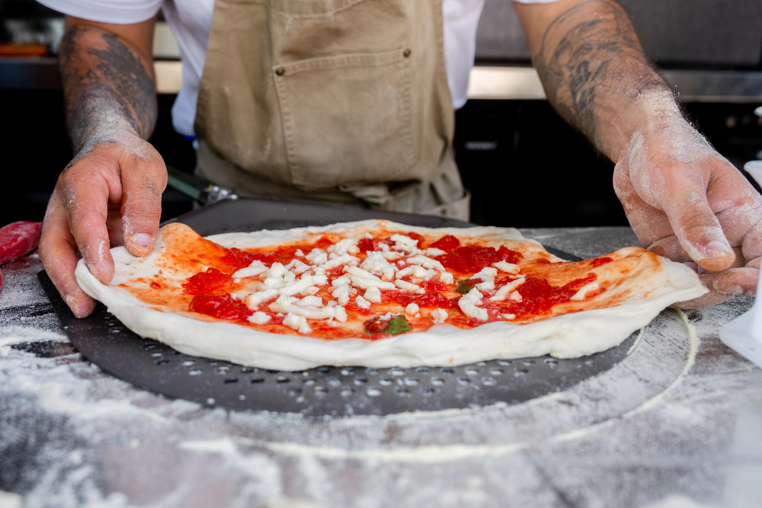 Person preparing a pizza with tomato sauce and cheese on a dough crust, on a floured surface.