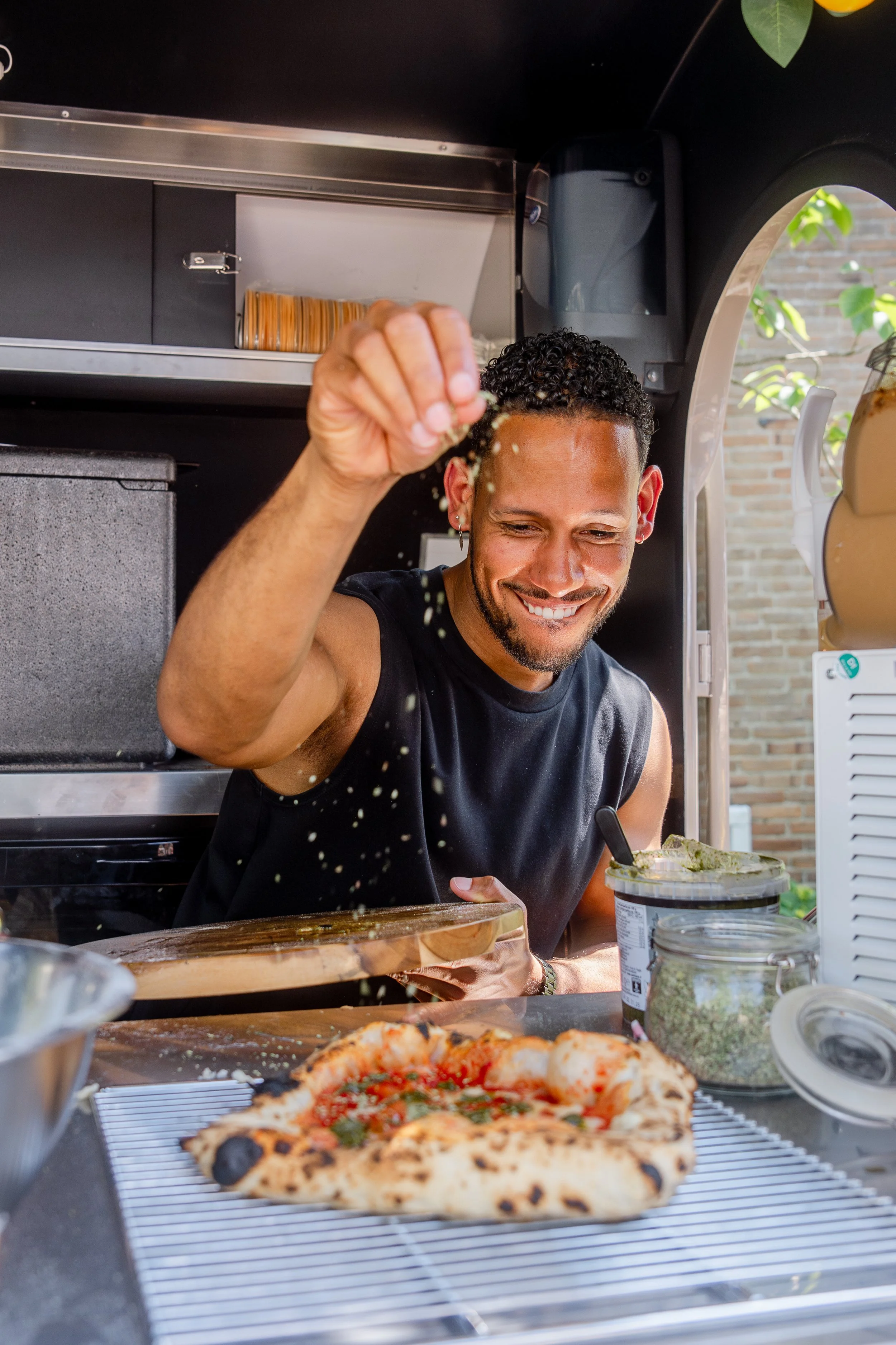 Man sprinkling herbs on a pizza in a food truck.