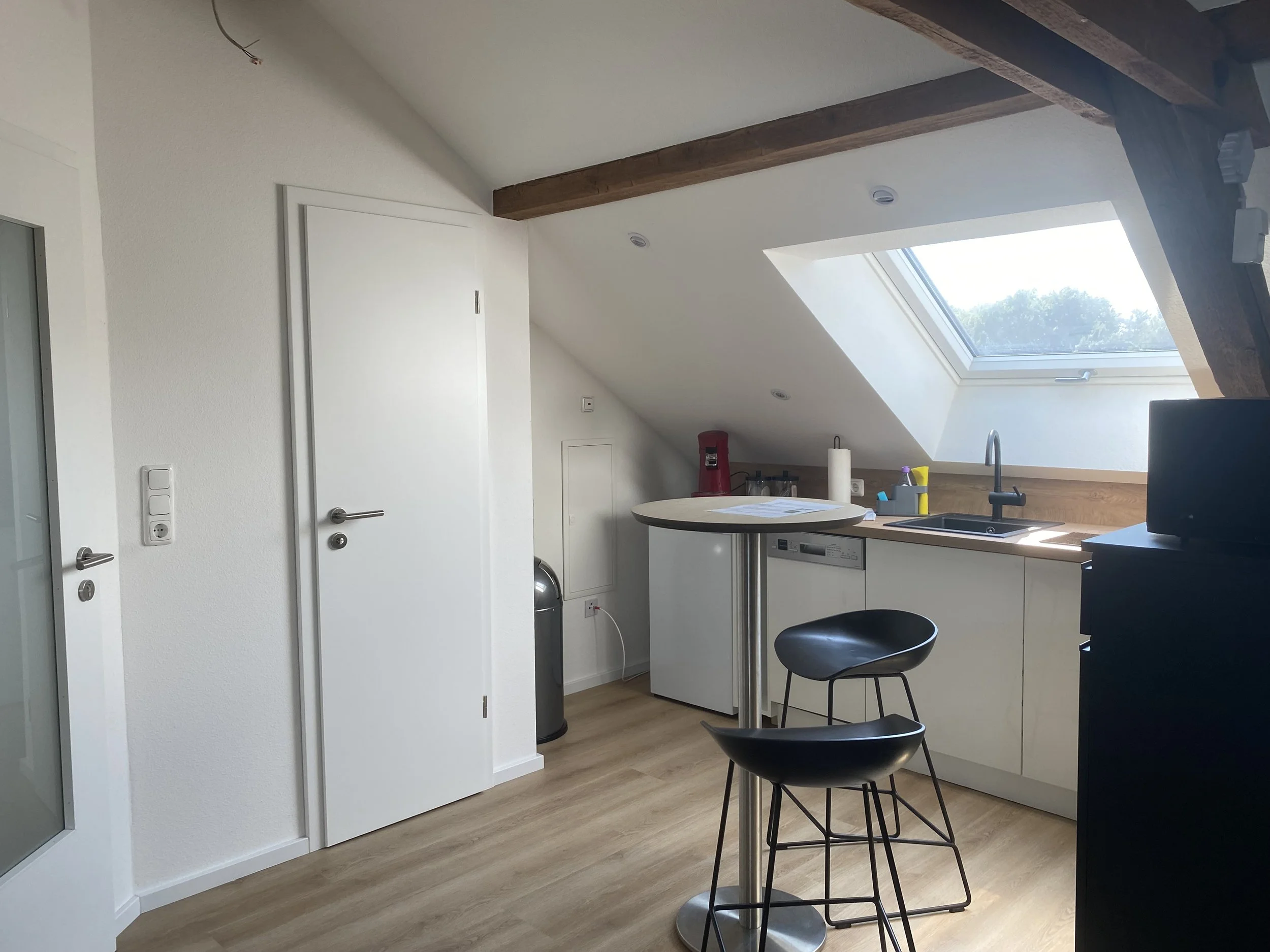 Küchenbereich mit Thron, Waschbecken unter Dachschrägen mit Dachfenster, weißen Schränken und Holzboden.