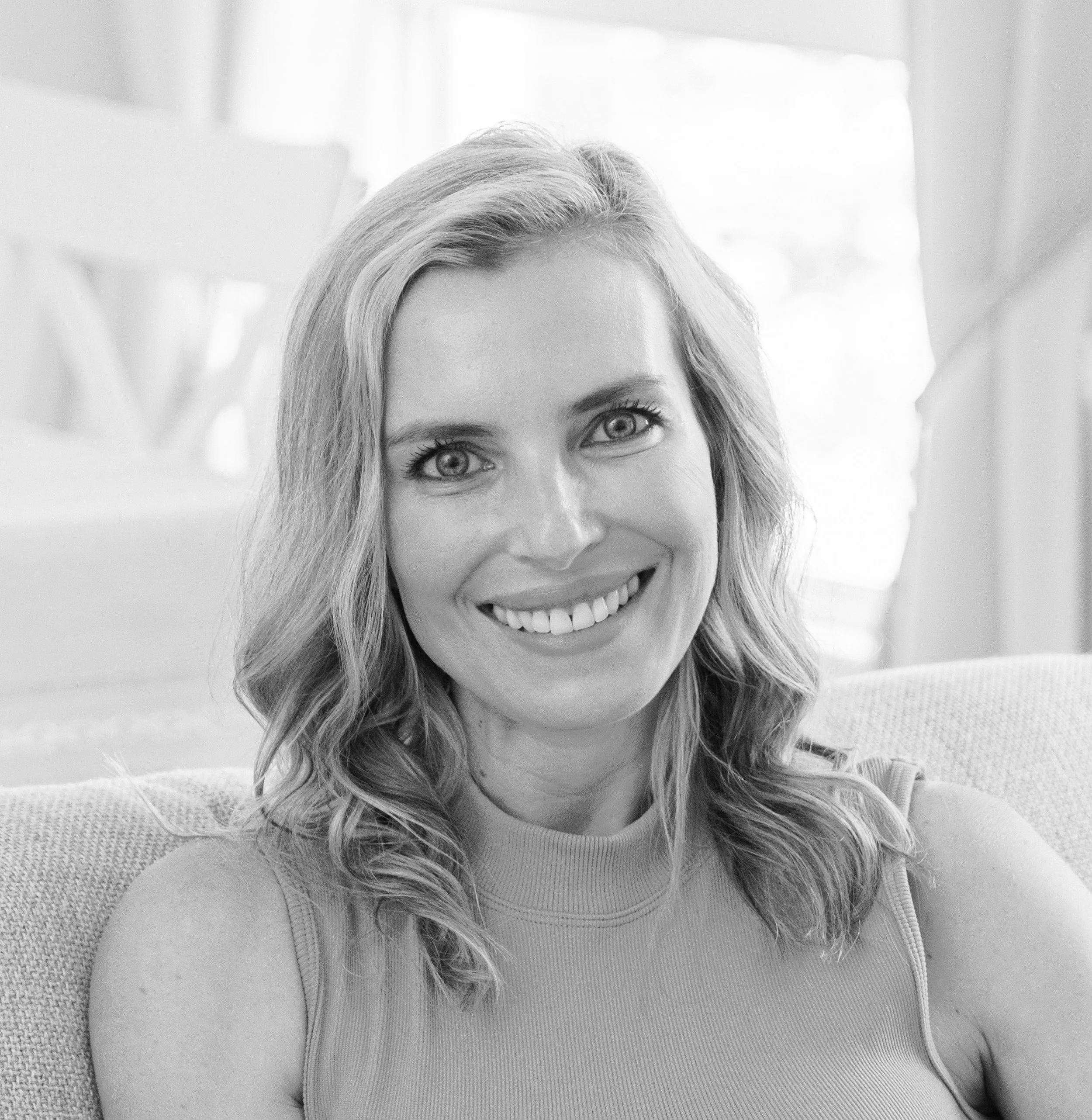 A woman with light-colored hair, smiling at the camera in black and white.