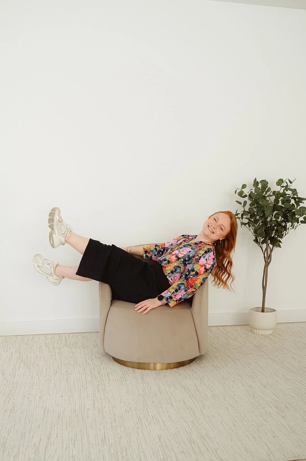 Vrouw met rood haar ligt op een beige fauteuil in een kamertje met witte muur en een plant in een witte pot op de achtergrond