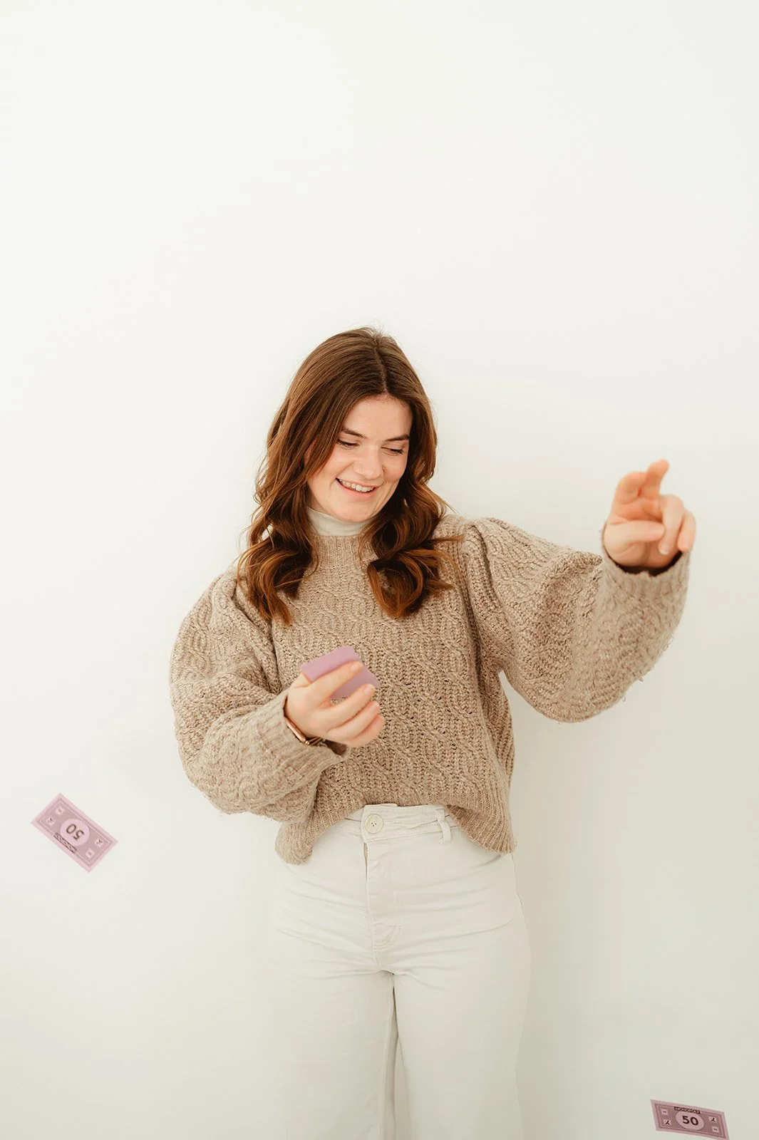 Vrouw die met een glimlach een roze spelletje vasthoudt, terwijl geldbiljetten van 50 euro naar beneden dwarrelen.