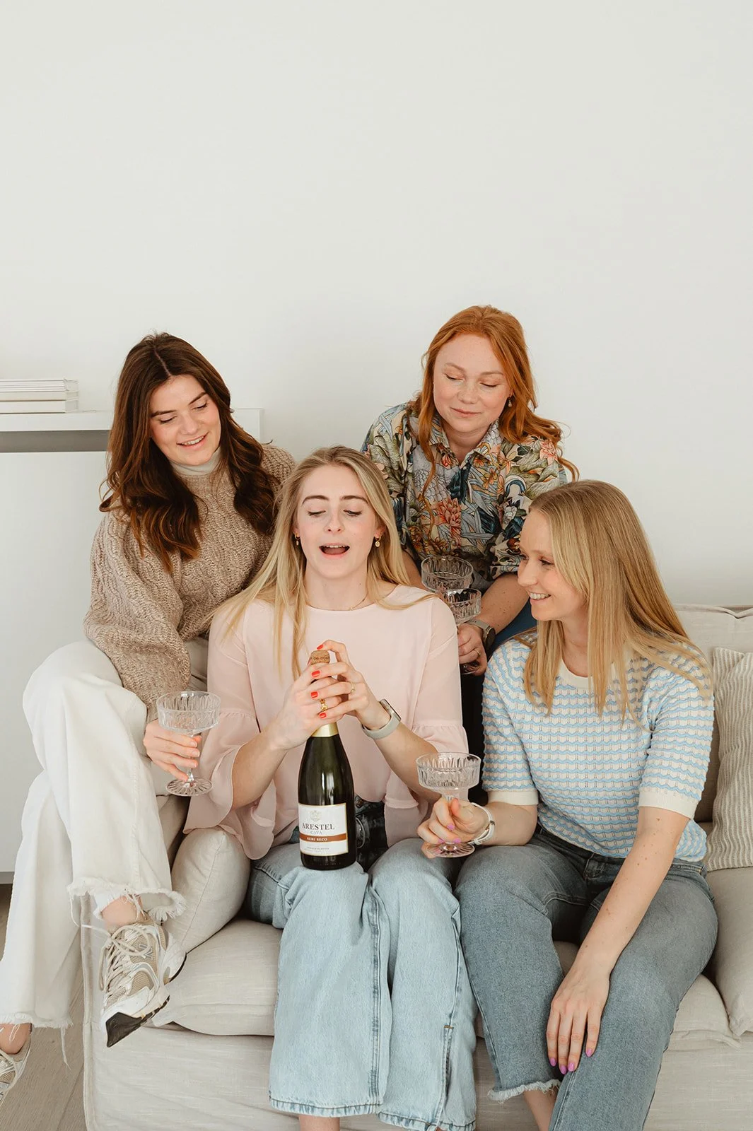Vijf vrouwen vieren een feestje op een bank, met een fles champagne en glazen in hun handen, op een gezellige kattige middag.
