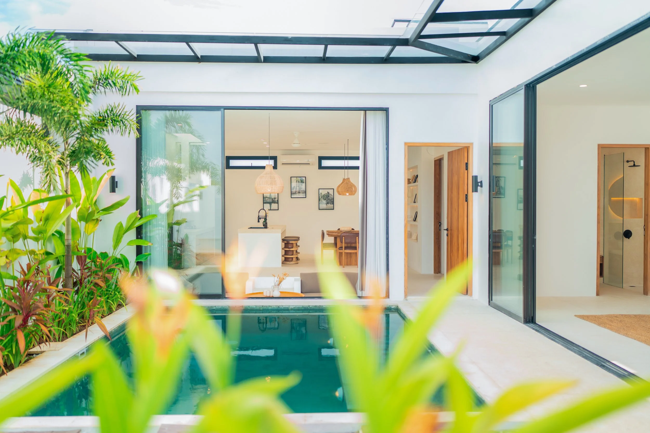 Modern house with large glass sliding doors and an indoor courtyard with plants and a swimming pool visible through the doors.