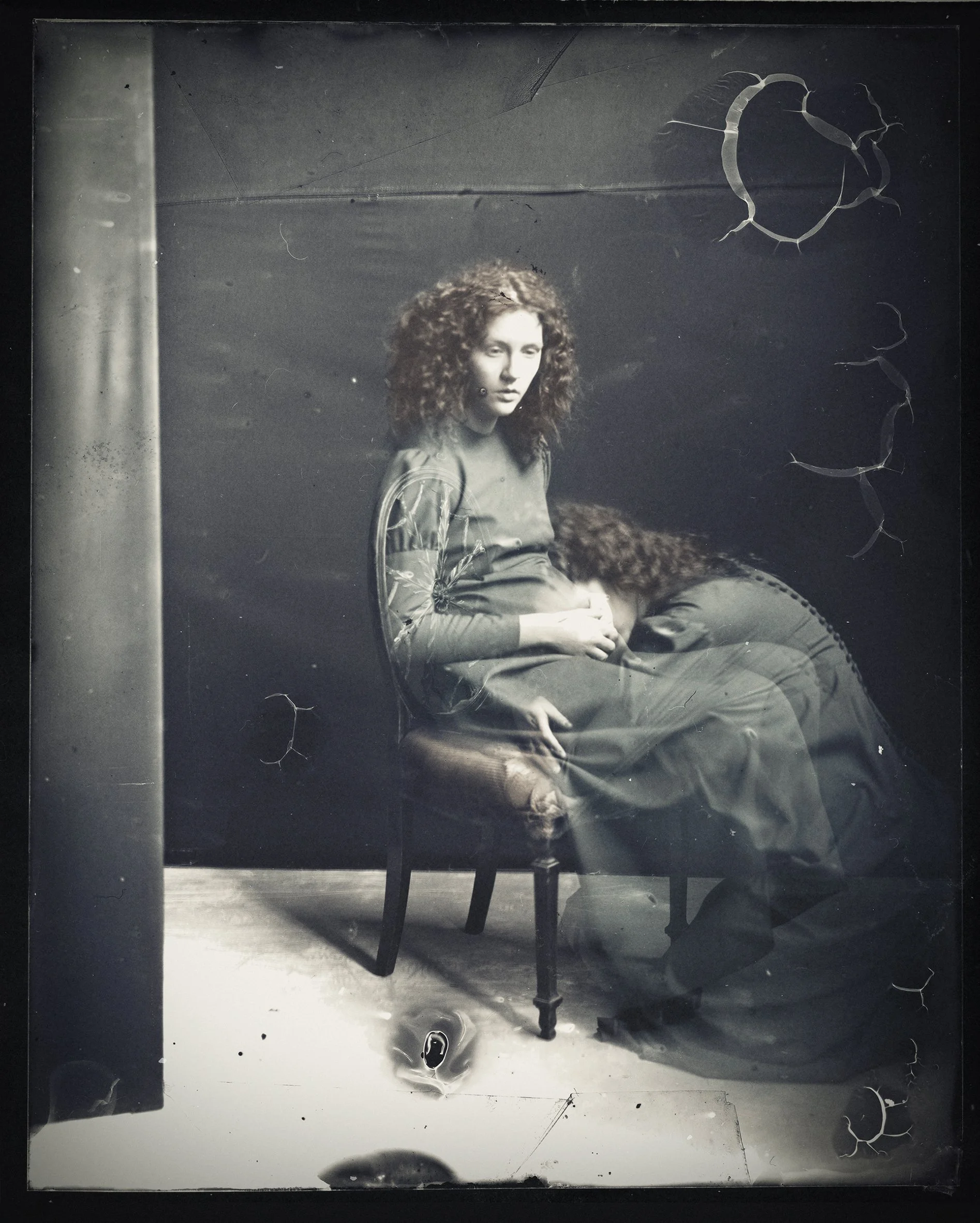 Black and white photograph of a woman with curly hair sitting on a vintage chair, with a dark background, some scratches, and marks.