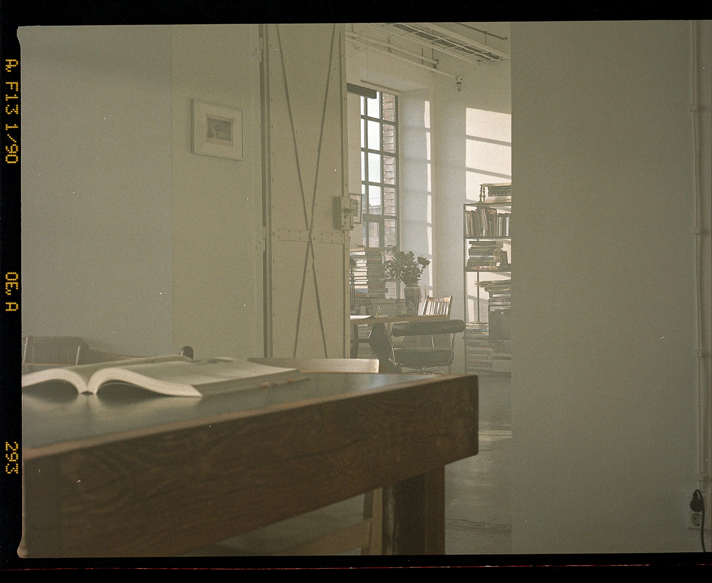 Sunlit office with bookshelves, a desk, and an open book on a table in the foreground.