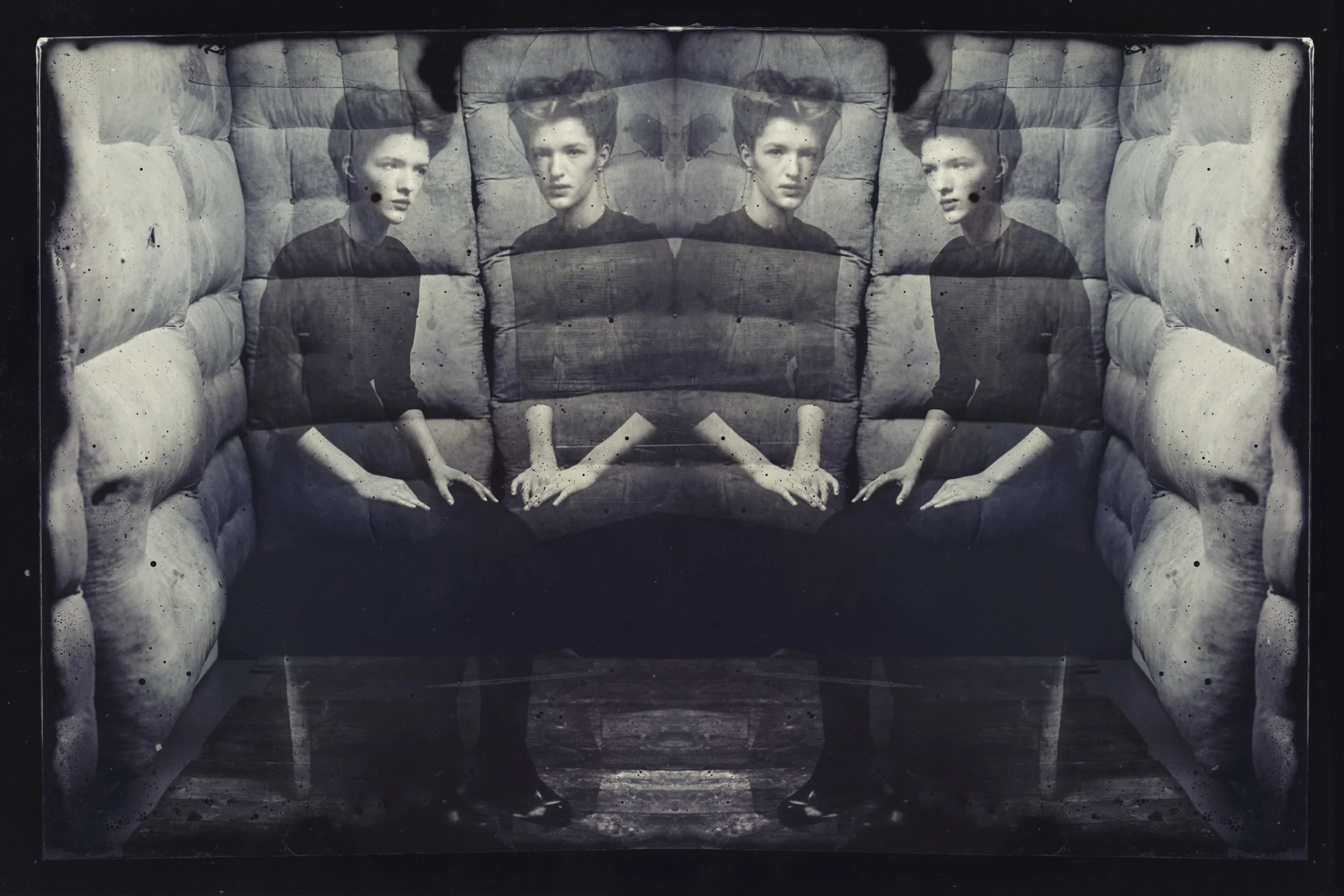 A black-and-white photo of a young man with short hair sitting on a tufted cushion and mirrored to create a symmetrical effect.