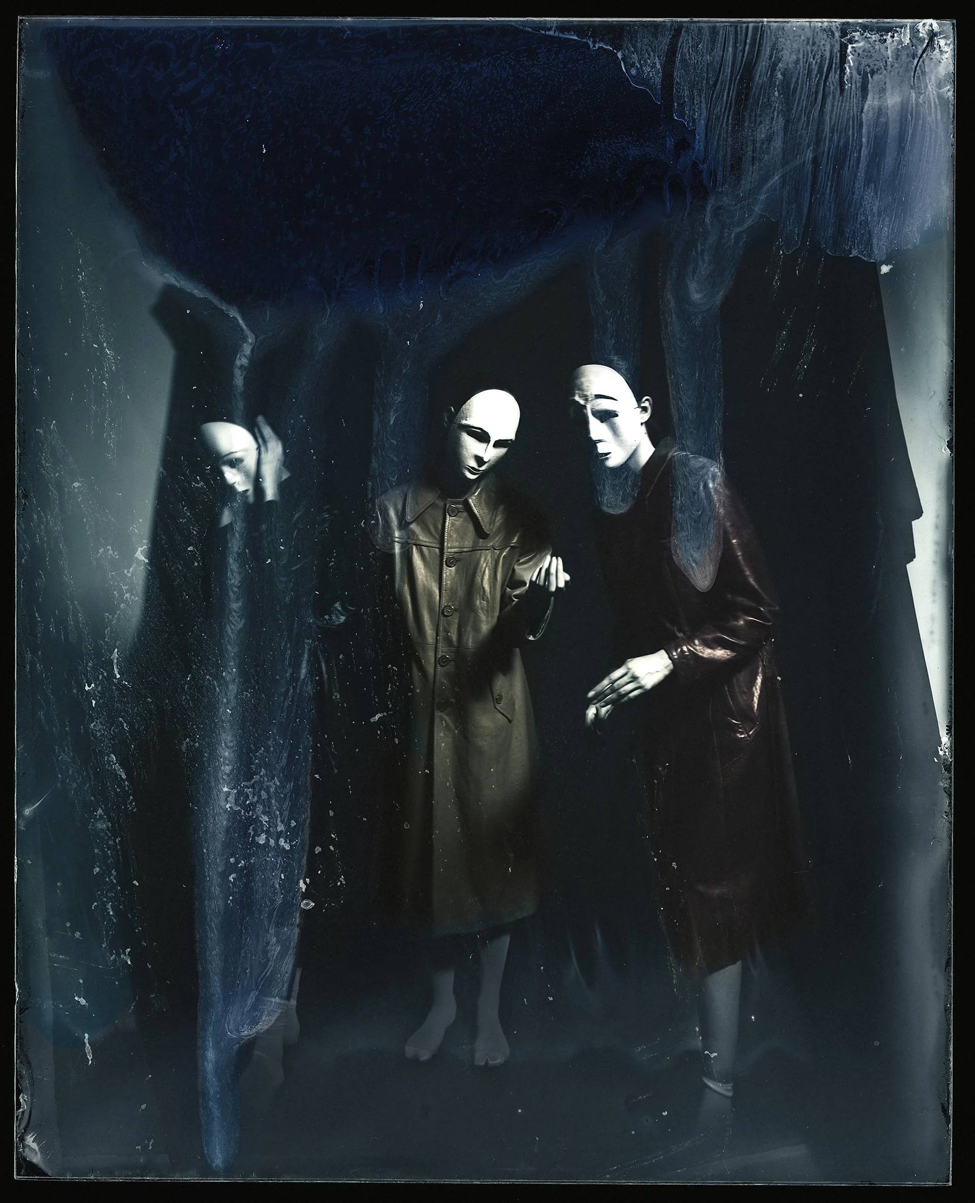 Three mannequins wearing leather coats displayed behind glass with a dark, textured background and reflected in the glass surface.
