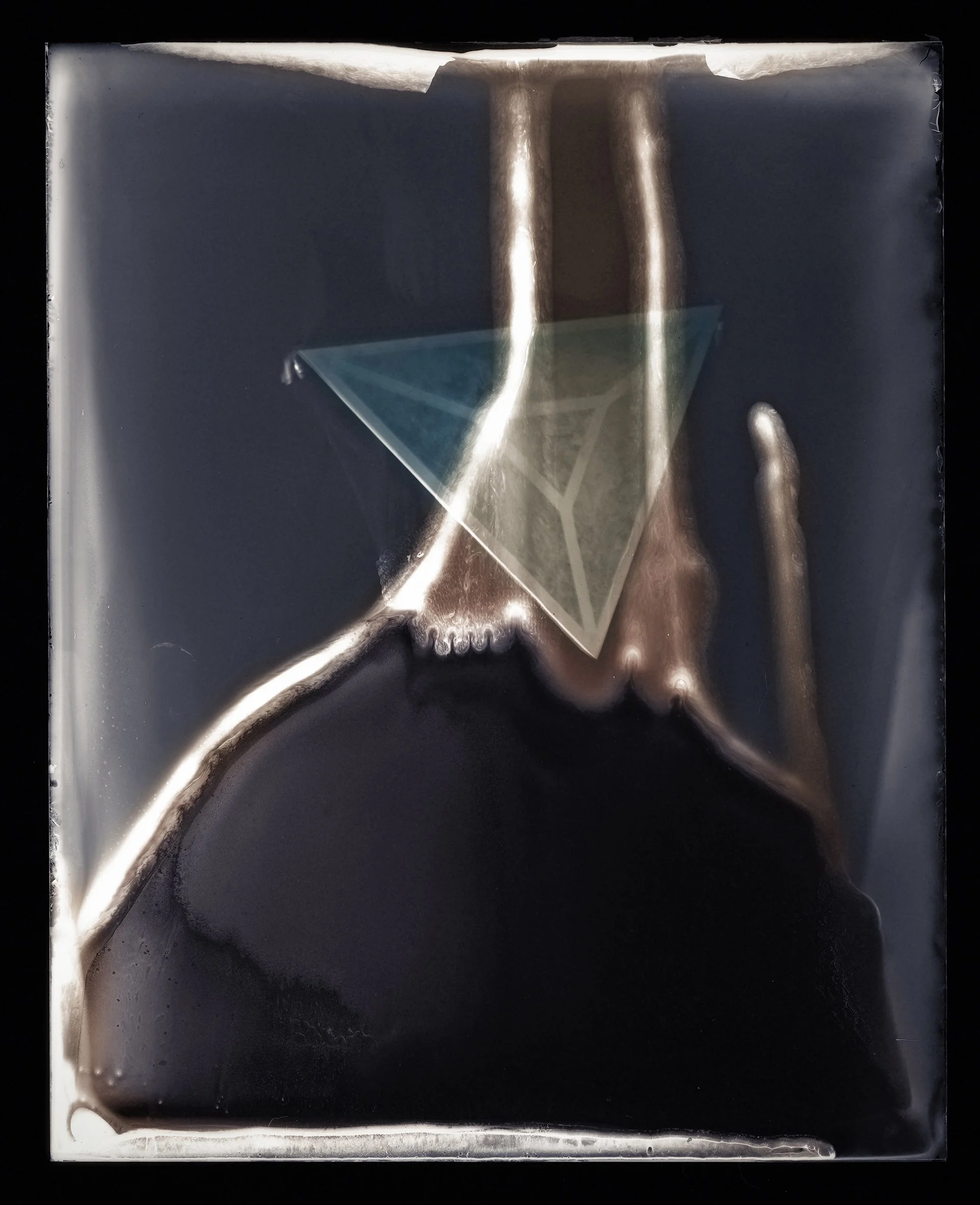 A dark rectangular metal sheet with a triangular glass or plastic piece suspended in the center, reflecting light.