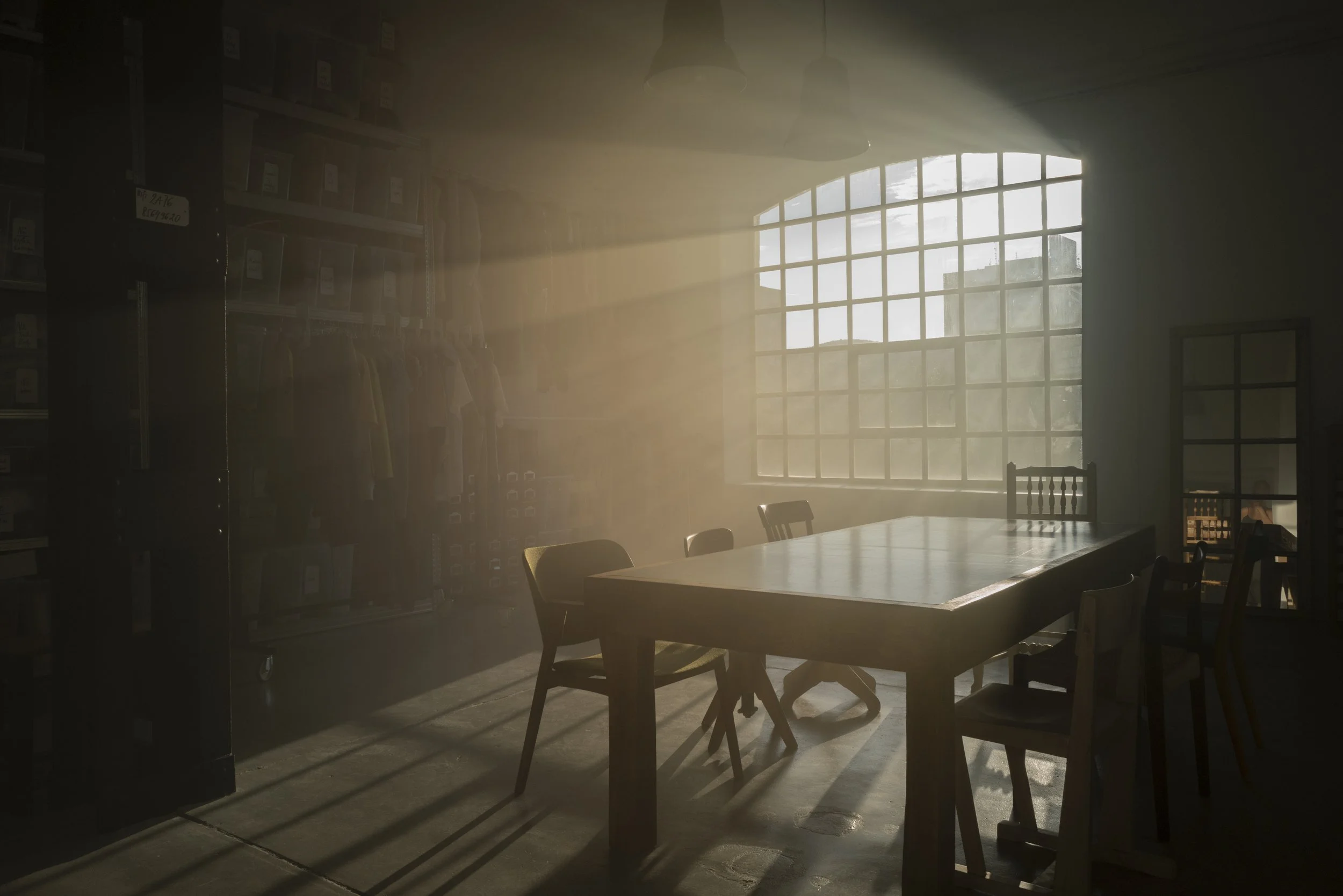 Sunlight streaming through a large window into a dimly lit room with a wooden table and chairs.