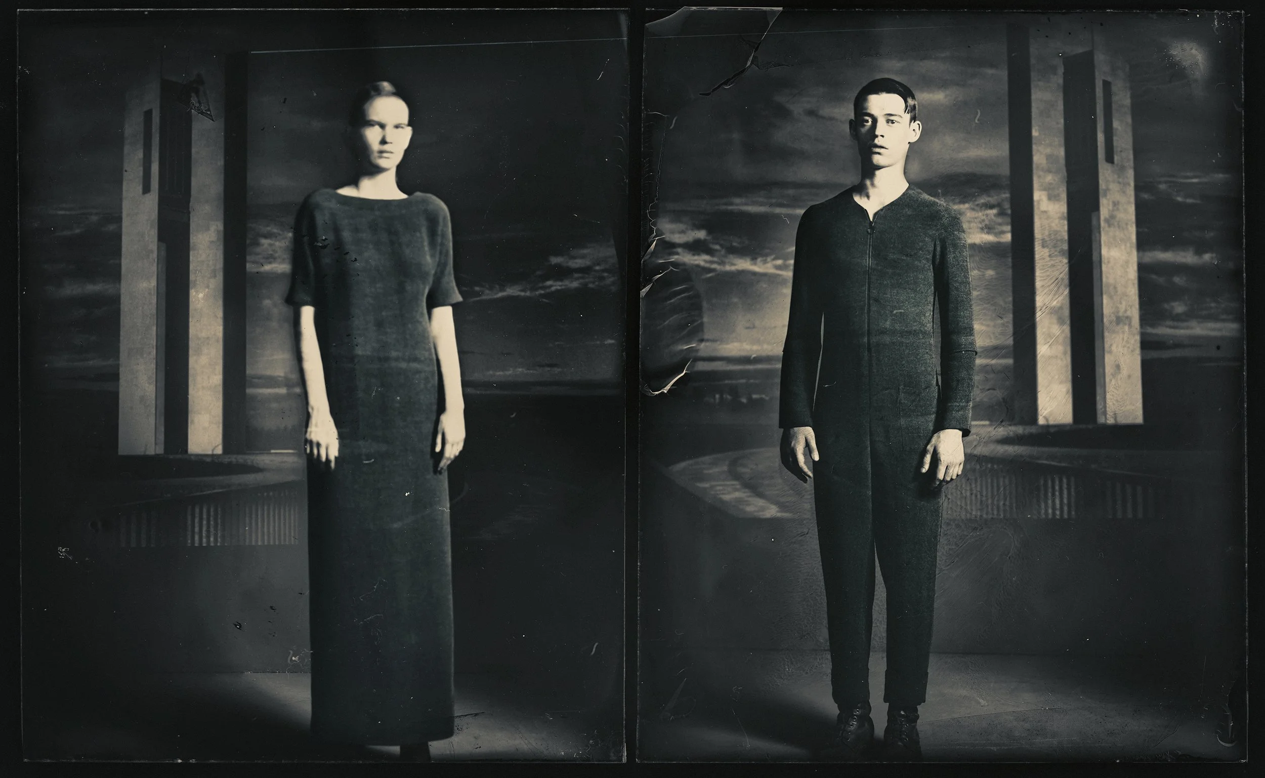 Black and white photo of two people standing in front of a cityscape background with large buildings, possibly at dusk or dawn.