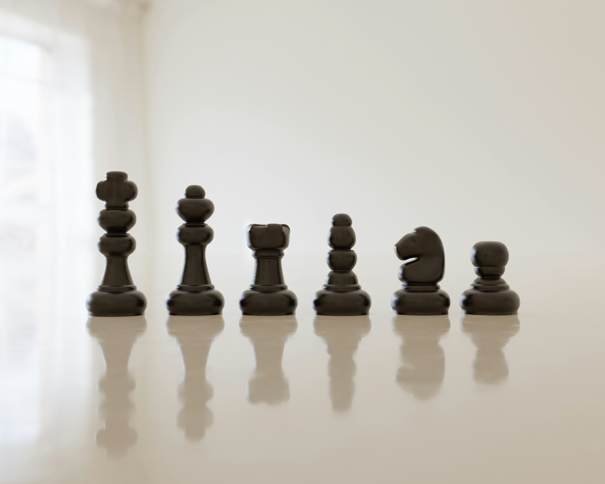 A set of black chess pieces arranged in a row on a white surface, with a light background.