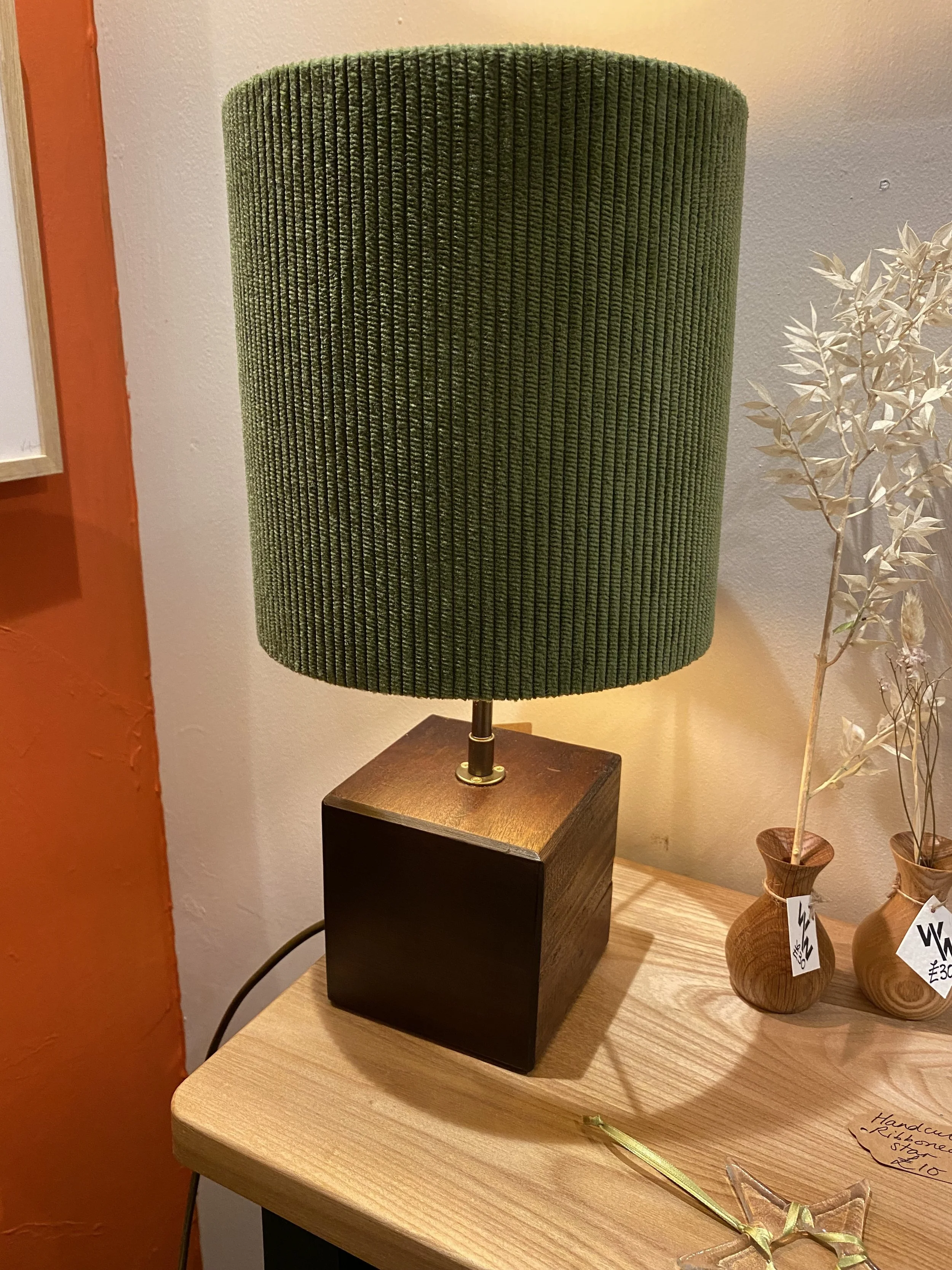 A green lampshade on a wooden table with two small vases containing dried plants beside it.