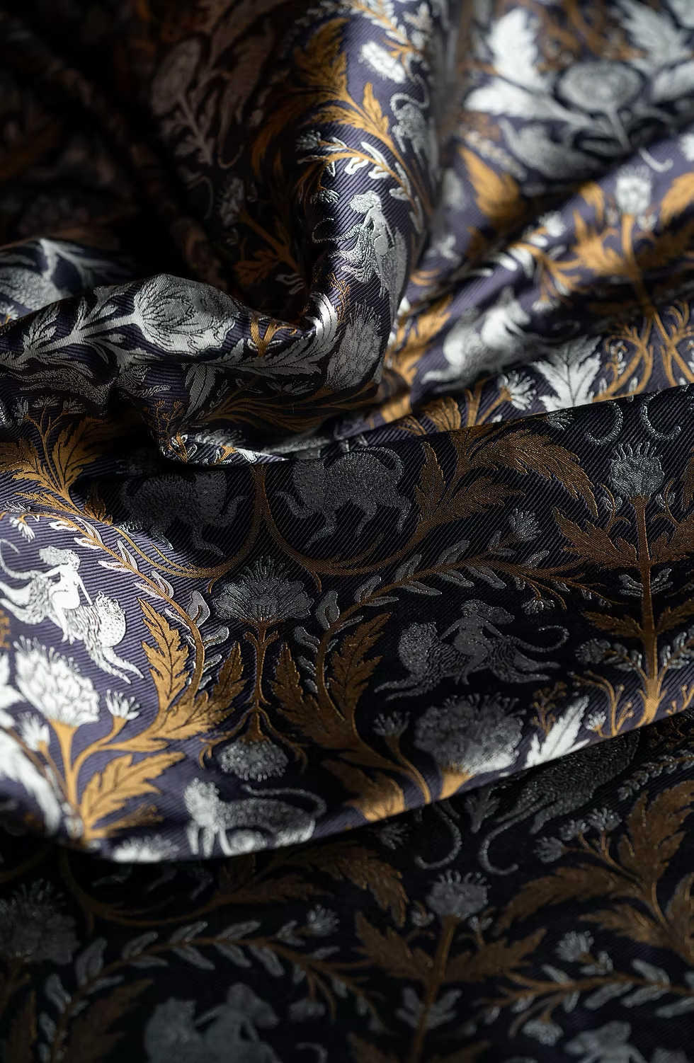 Close-up of intricately woven fabric with a black, gold, and silver floral pattern, featuring detailed leaves and flowers.