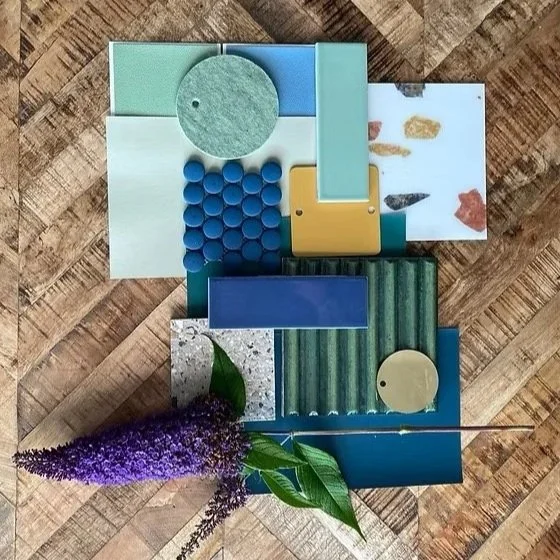 Flat lay of assorted objects including a round felt pad, a cluster of blue pills, a small blue rectangular container, a yellow rectangular block, a sheet with small images, a purple bouquet of flowers with green leaves, a round beige object, and a th