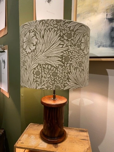 Table lamp with a carved wooden base and a floral patterned shade, placed on a wooden surface in an art or decor display setting.