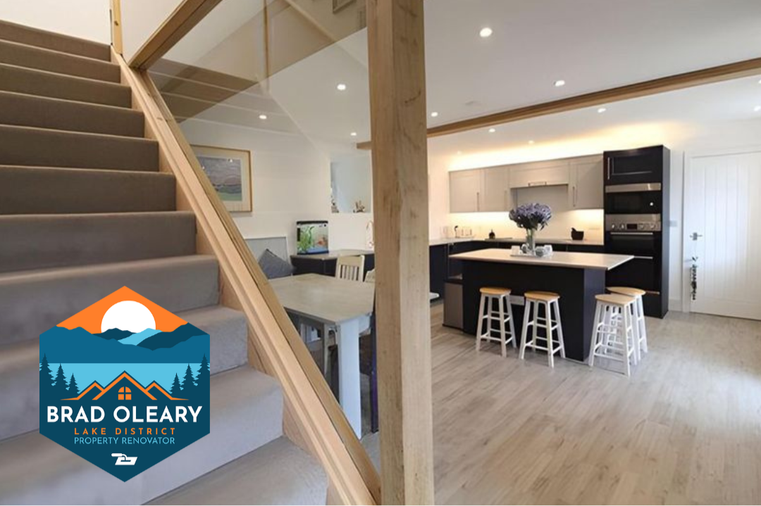 Open-concept kitchen and living area with wooden stairs, light wood flooring, kitchen island with stools. Meet builder & lime plaster specialist Brad O'Leary, Lake District Property Renovator at the Home Interiors & Renovation Exhibition 2026.