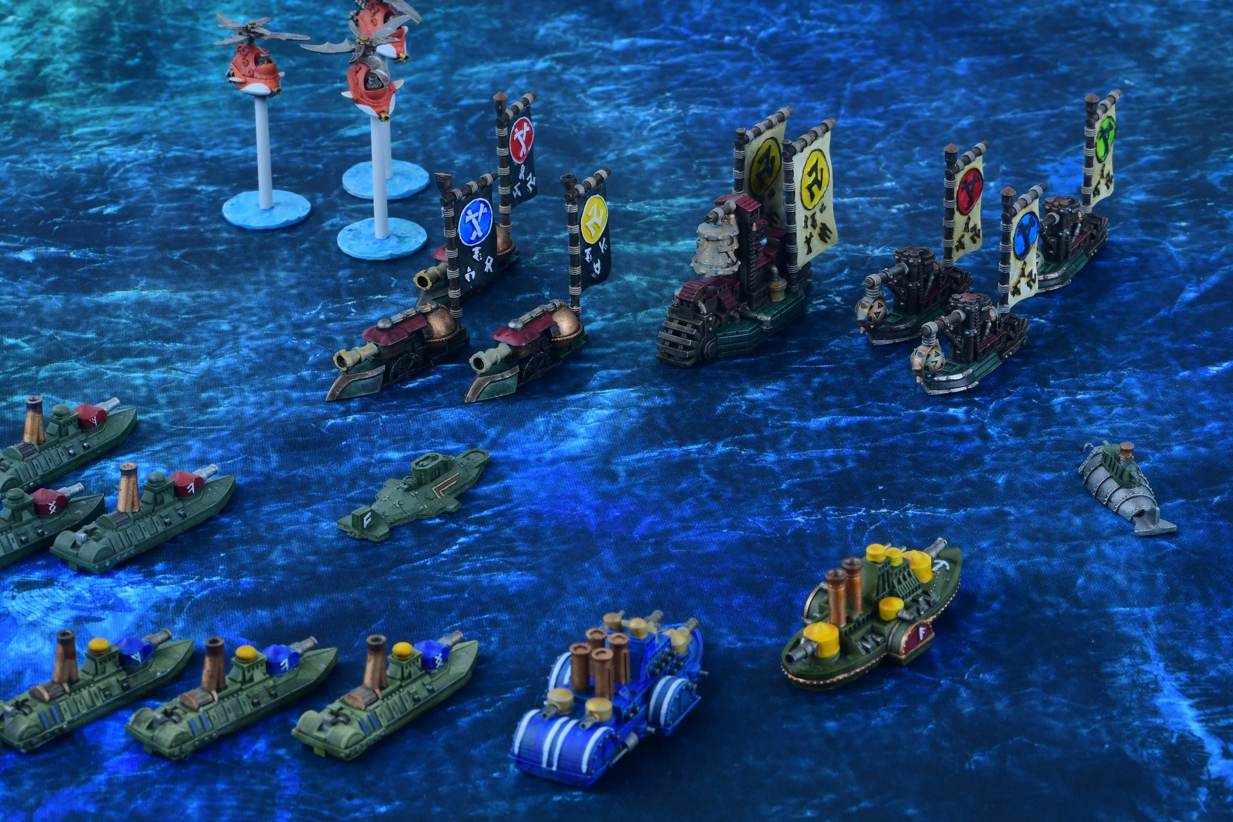 Miniature ships and boats on a blue textured surface, arranged as a naval fleet or diorama.
