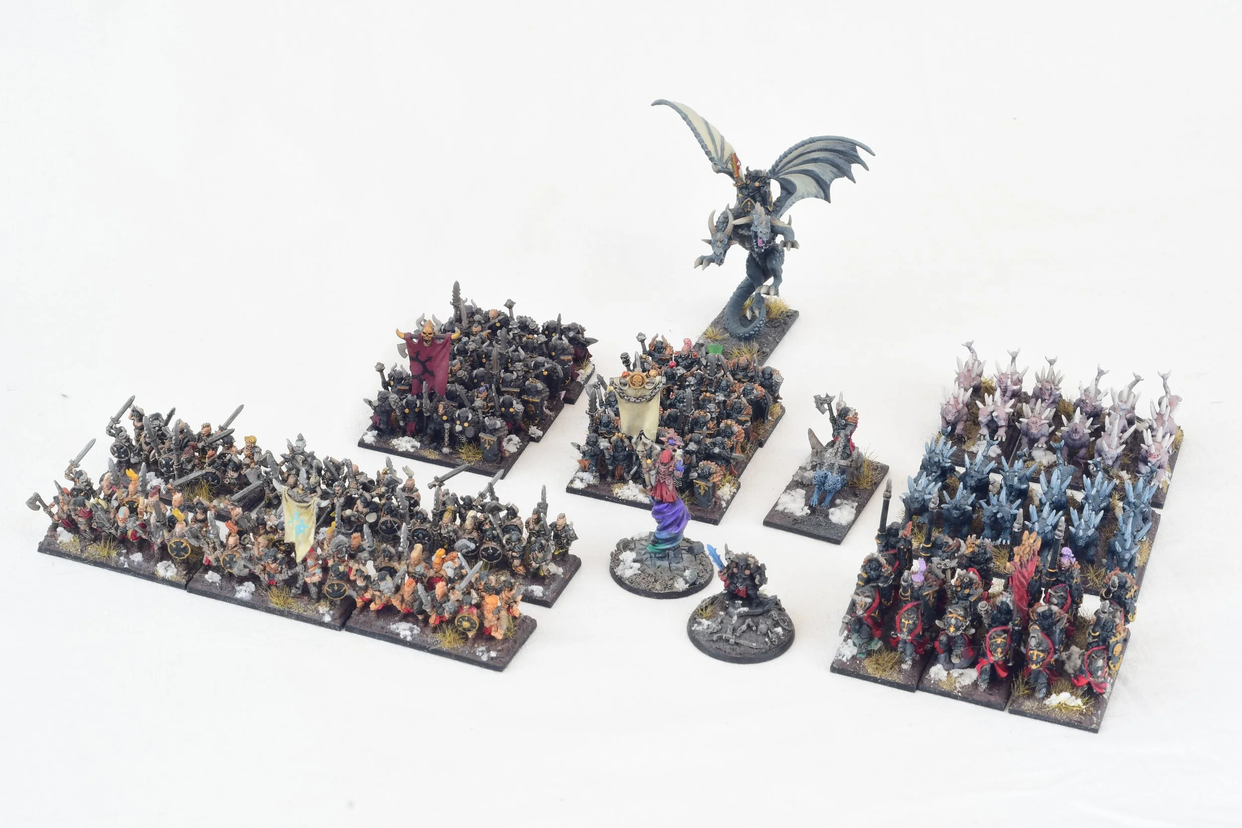 Miniature fantasy war game figures arranged on a white background, including soldiers, a dragon, and other mythical creatures.