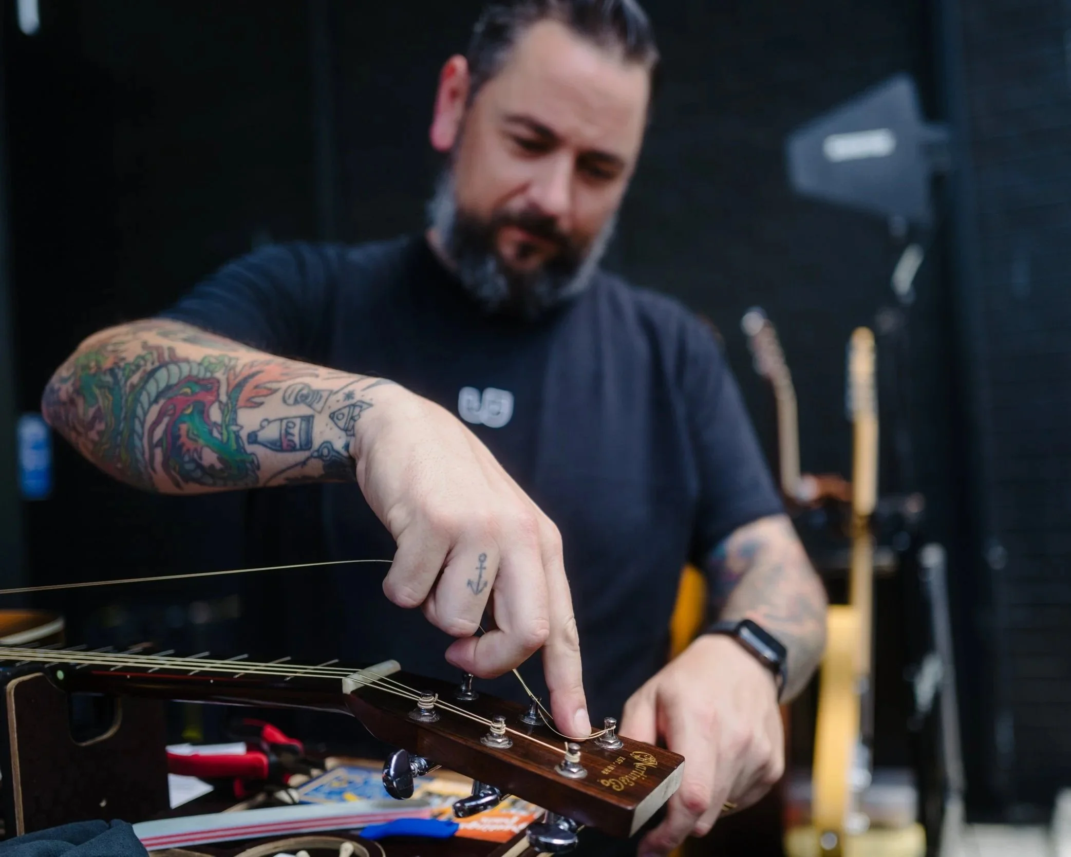 A man with tattoos on his arm tuning a guitar in a workshop.
