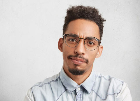 A man with curly hair and glasses making a confused or skeptical facial expression.