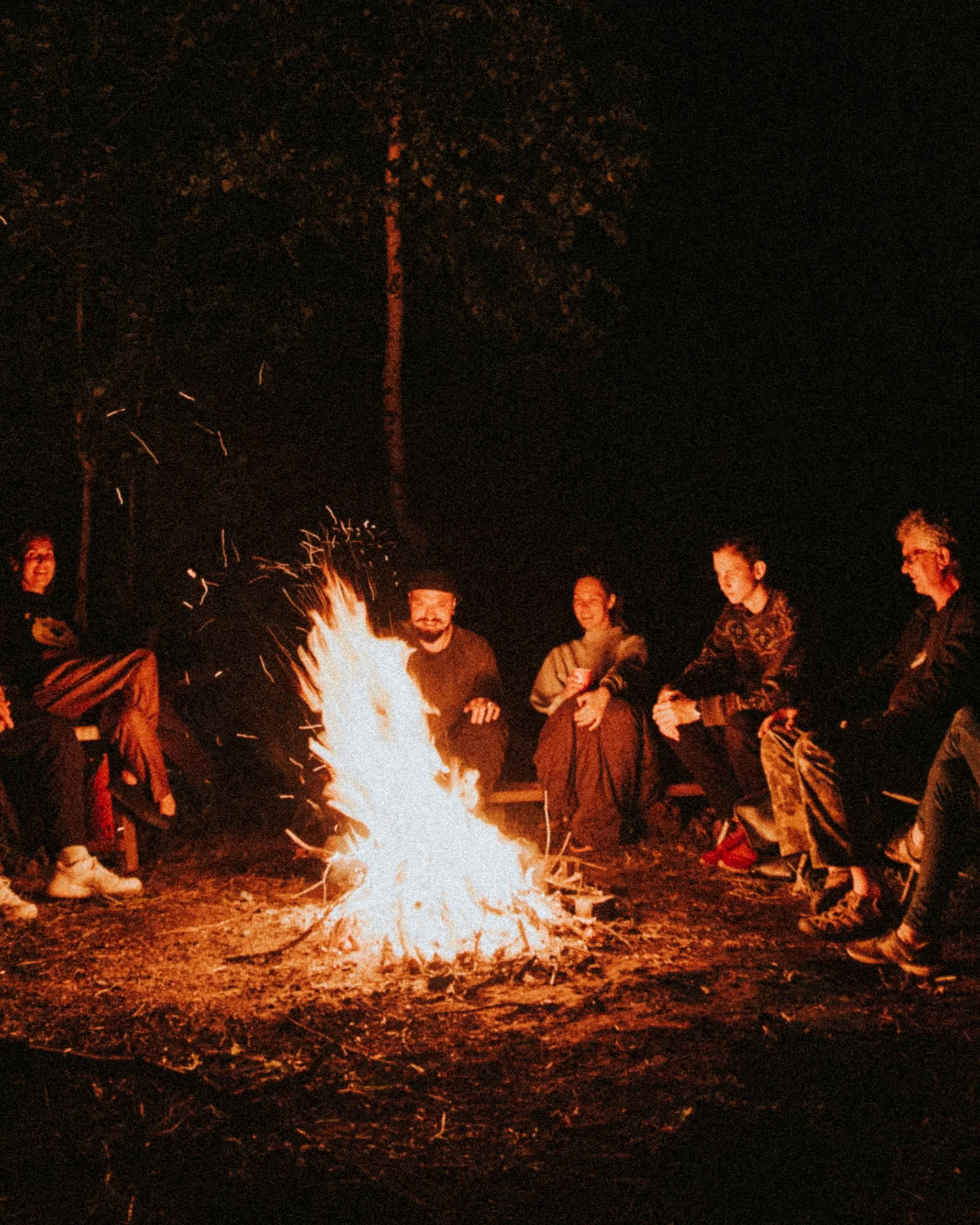 Groupe de personnes assises autour d'un feu de camp en plein air la nuit.