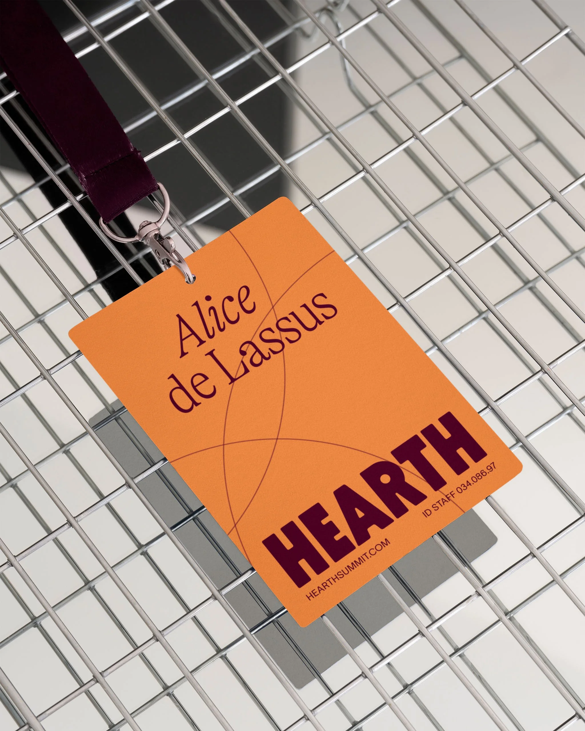 Badge orange avec le nom Alice de Lassus, attaché à une lanière violette, posé sur une grille métallique.