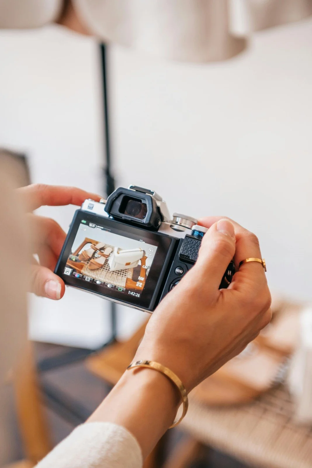 Une personne tenant un appareil photo numérique, prenant une photo d'un sac beige sur une table en bois.