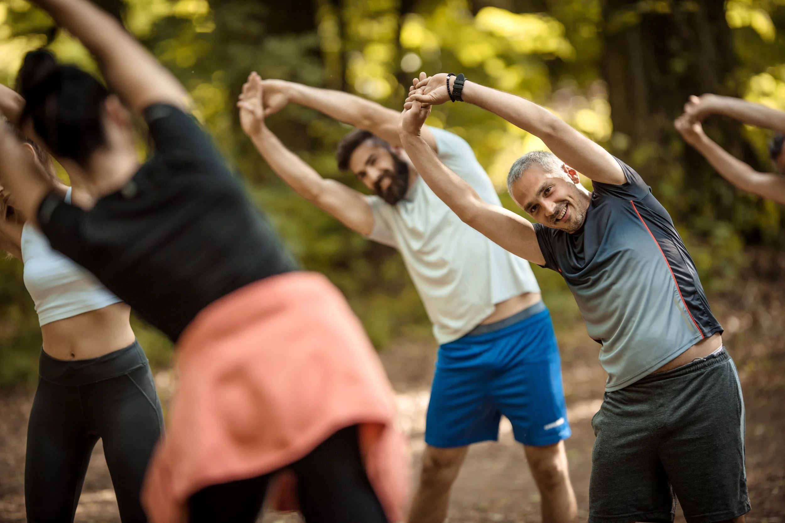 Group-of-happy-athletes-stretching-their-arms-with-an-instructor-in-nature.-874312922_7360x4912.jpg