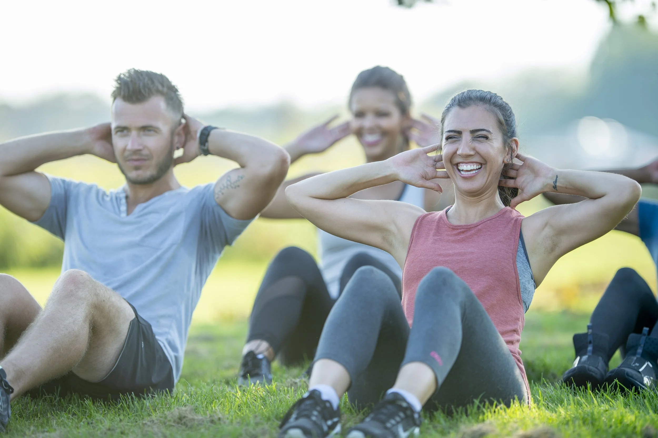 Menschen beim Outdoor-Workout, sitzend auf Gras, lachend und Übungen machend