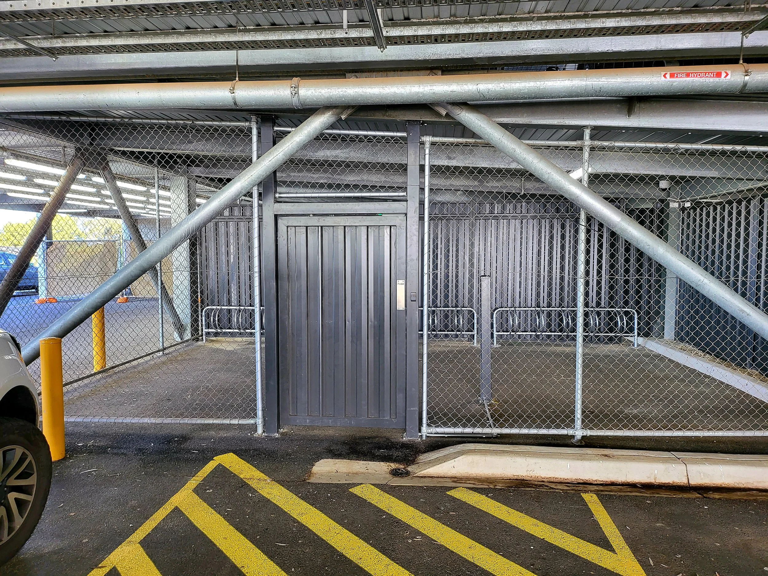 Parking garage with a fenced-off bike storage area, locked metal gate, and yellow striped pavement.