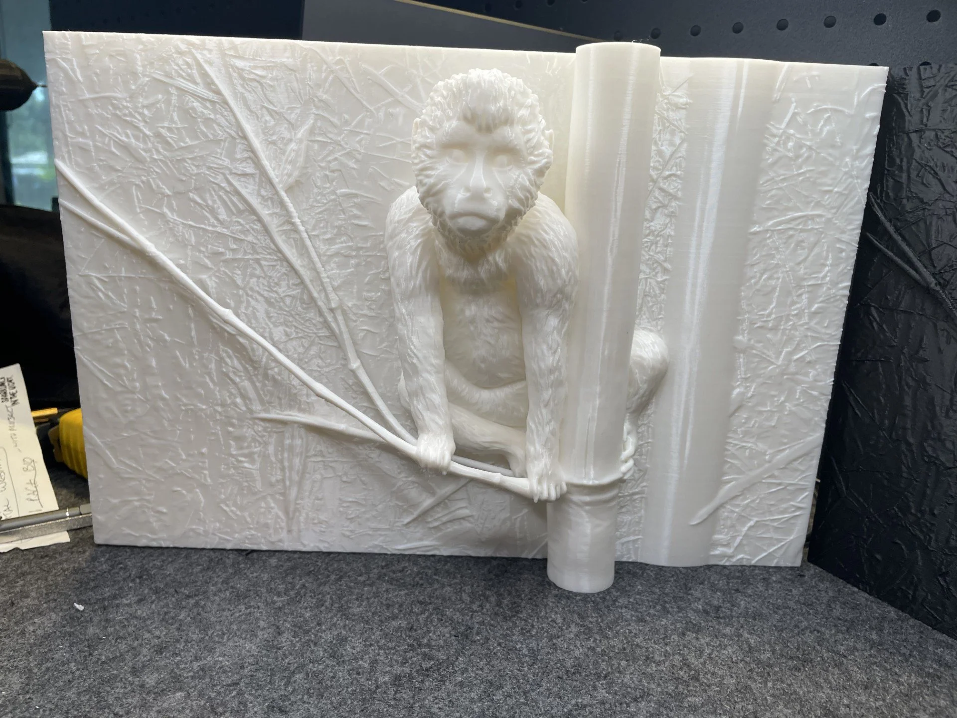 White 3d print  sculpture of a monkey sitting on a textured background with bamboo leaves