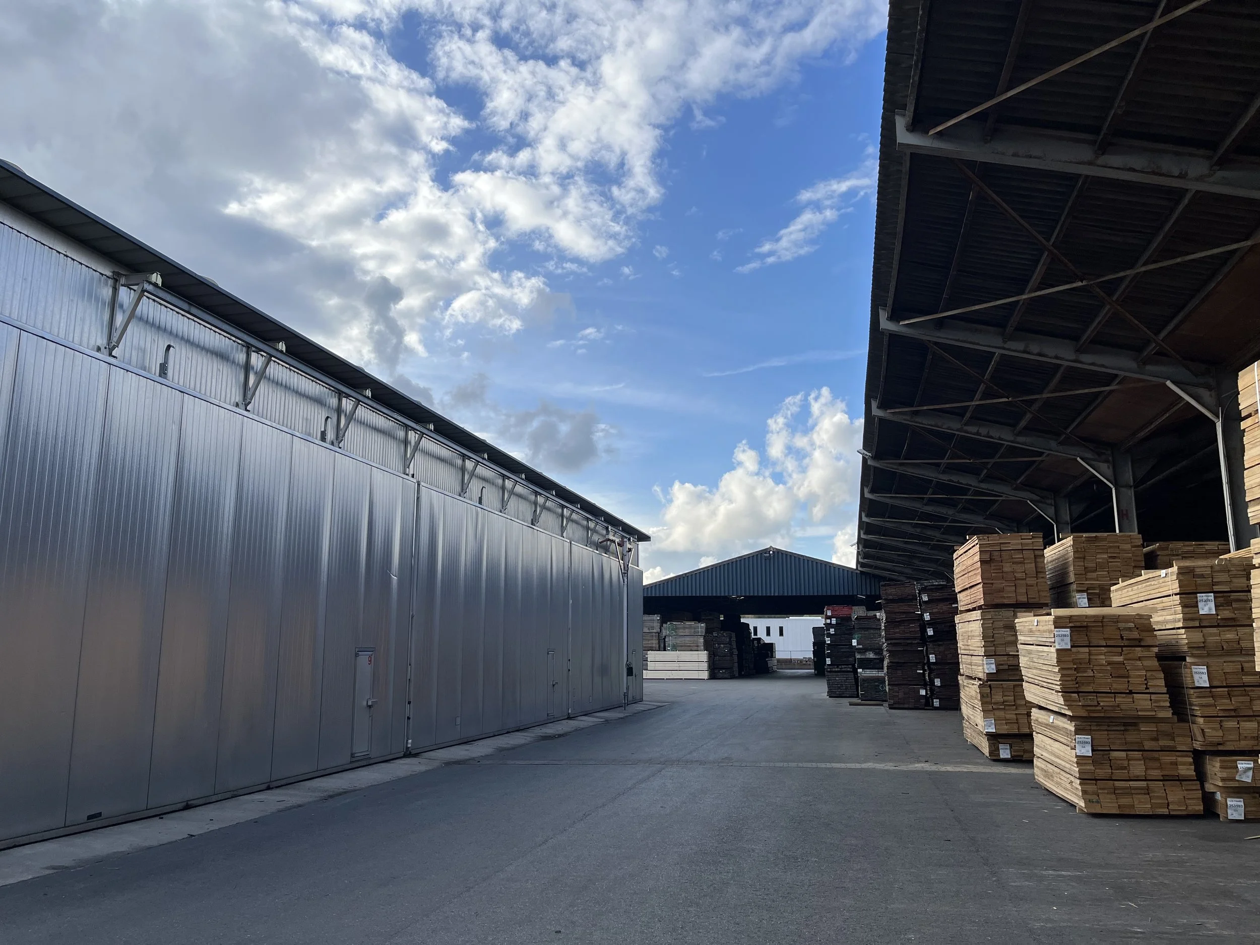 Een zwart-wit foto van een grote, metalen magazijn met meerdere schuifdeuren, een betonnen oprit en een grasrand op de achtergrond.