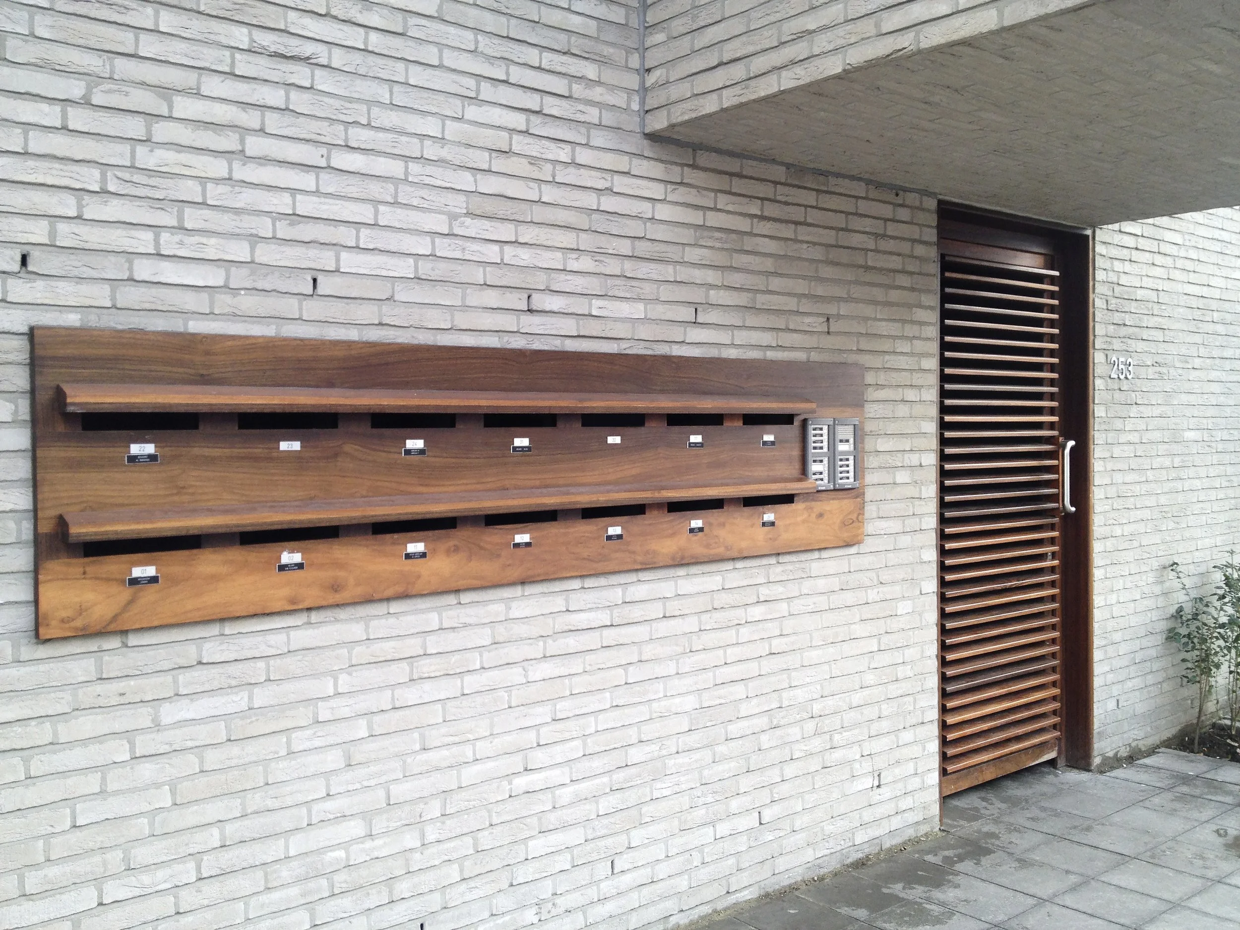 Postbussen met meerdere vakken en een meldpost naast de deuren van een modern gebouw met bakstenen muren.