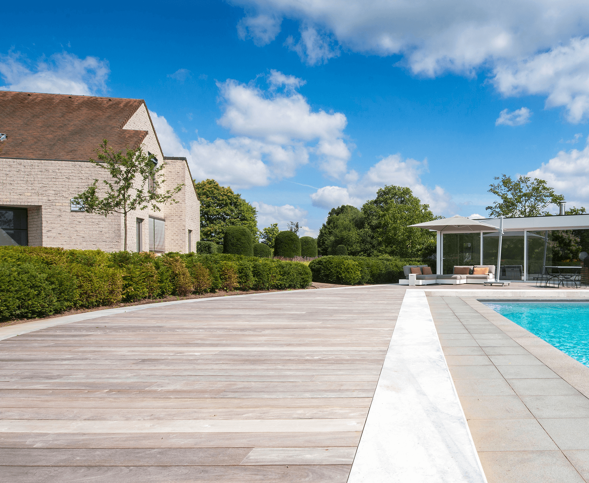 Moderne achtertuin met zwembad, houten terras, zitgedeelte met banken, parasol en ommuurde tuin.