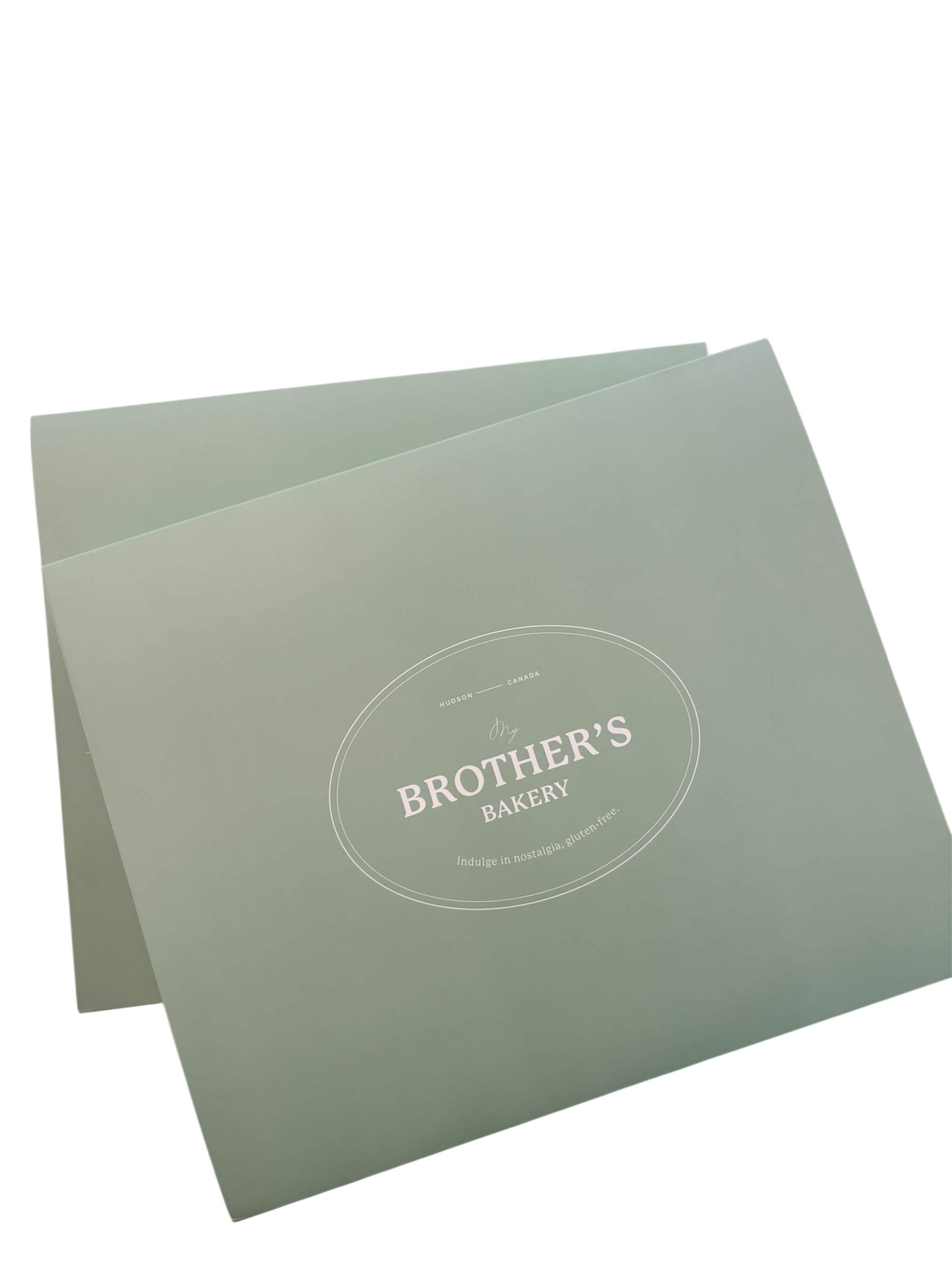 A pastel green bakery box with white text that reads "Our Brother's Bakery, Indulge in nostalgia, gluten-free," from Hudson, Canada.