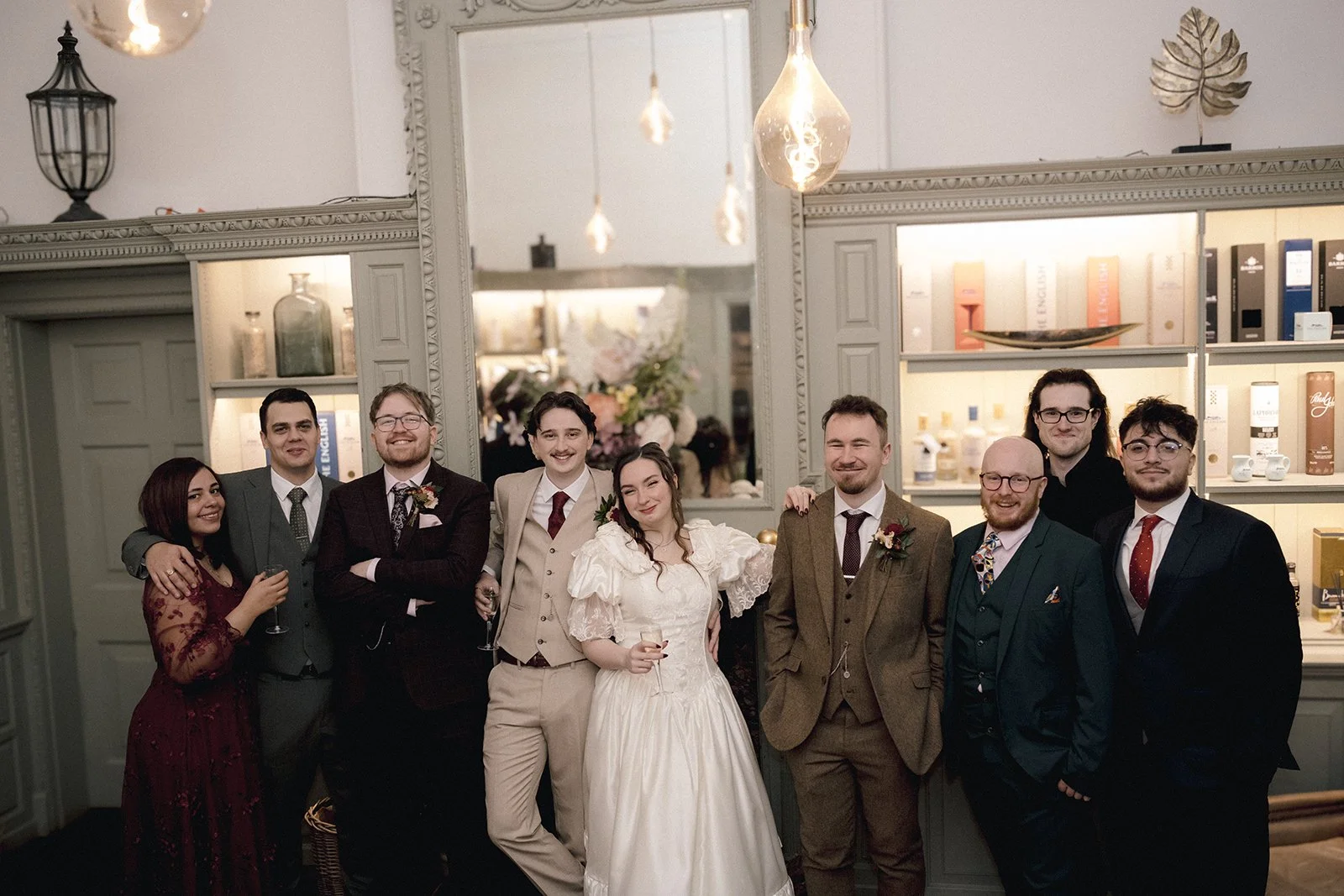 Wedding party at a wedding celebration, with some holding glasses of champagne, standing inside a decorated room. Caistor Hall, Norwich.